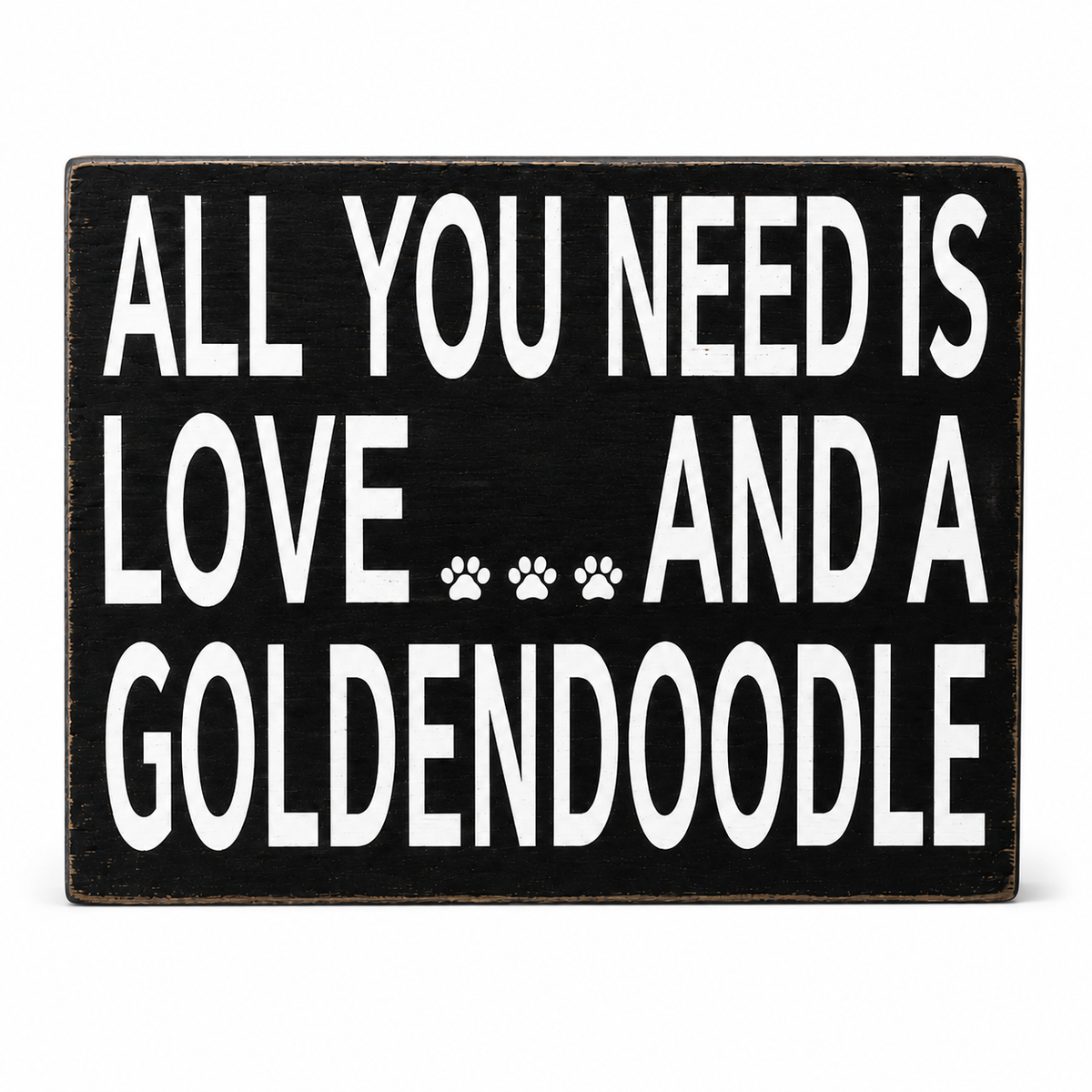 A rectangular black wooden sign with distressed edges featuring the white text 'ALL YOU NEED IS LOVE.