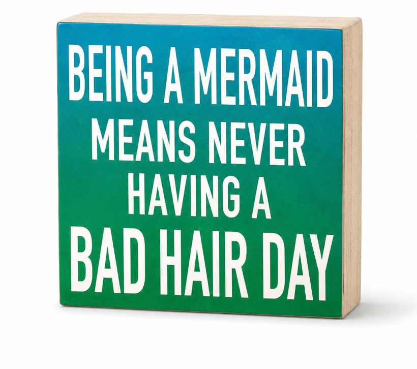 A square decorative block sign with a teal-to-green gradient face and white text reading 'BEING A MERMAID MEANS NEVER HAVING A BAD HAIR DAY', shown on a clean white background.