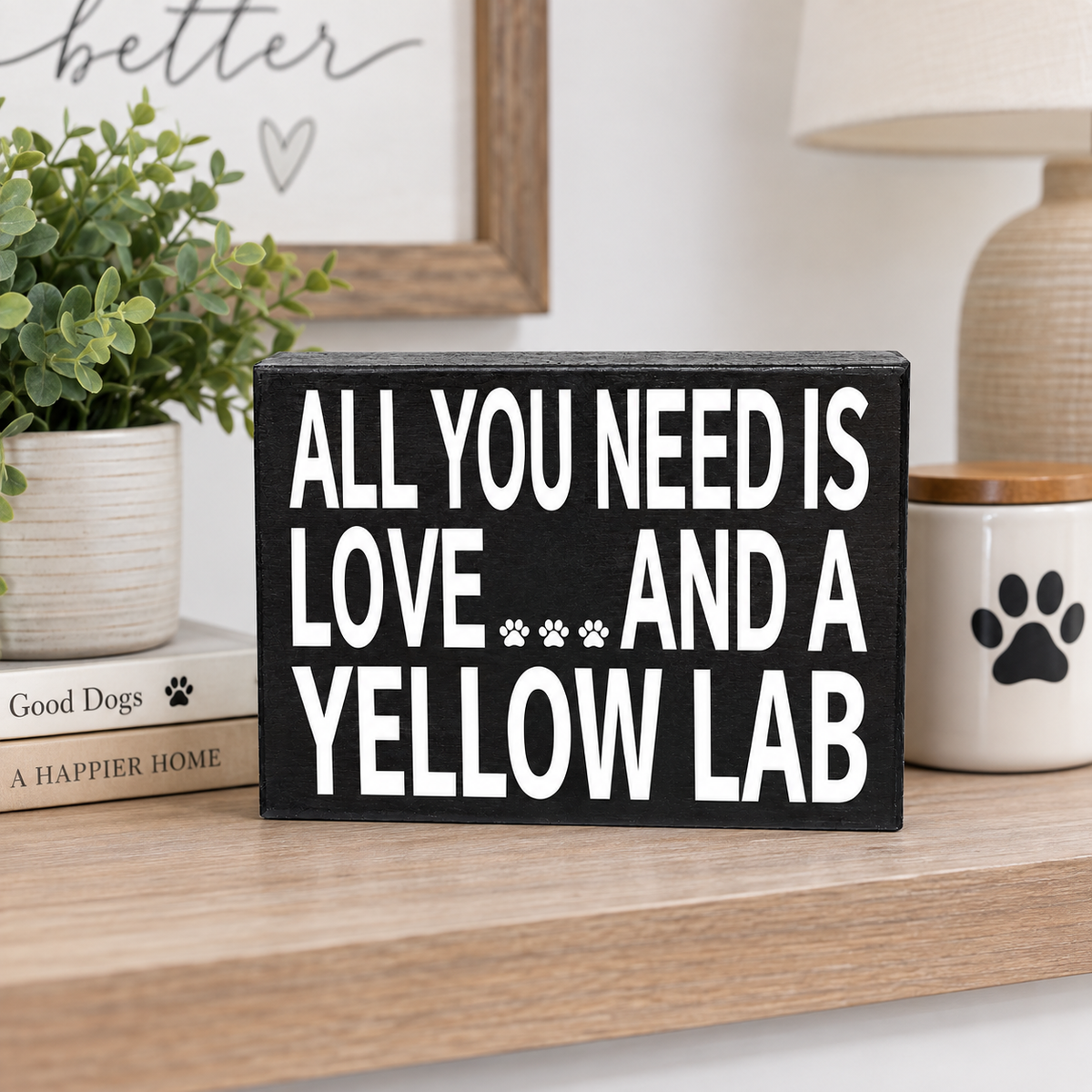 A rectangular black wooden sign with bold white text reading 'ALL YOU NEED IS LOVE.