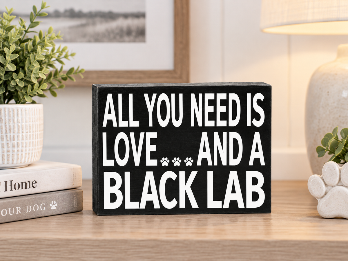 A rectangular black wooden sign with bold white text reading 'ALL YOU NEED IS LOVE.