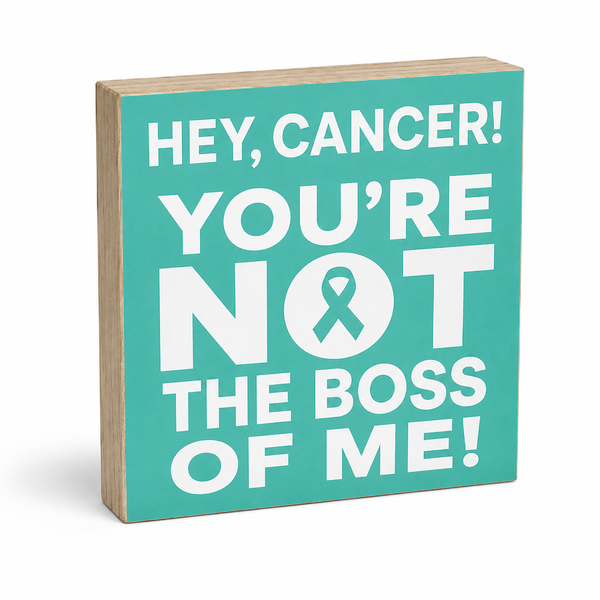 A square wooden sign with a turquoise front and natural wood edges, featuring the text 'HEY, CANCER! YOU'RE NOT THE BOSS OF ME!' in bold white lettering with a teal ribbon symbol inside the letter O.