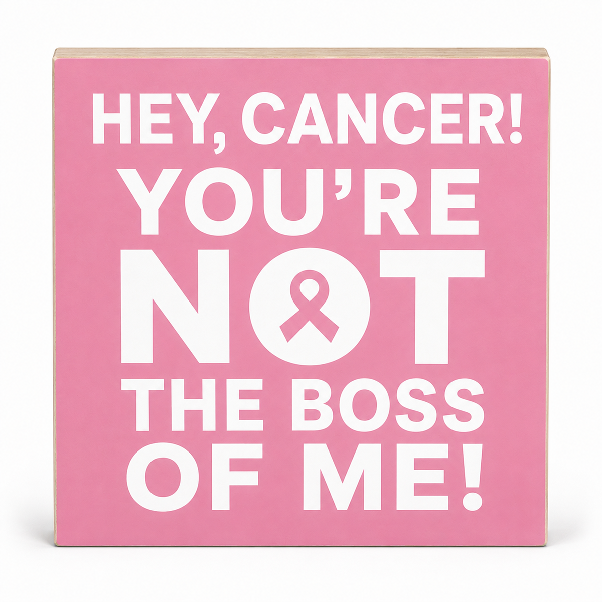 A square pink decorative sign with bold white text reading 'HEY, CANCER! YOU'RE NOT THE BOSS OF ME!' and a pink awareness ribbon inside the letter O, shown on a white background.