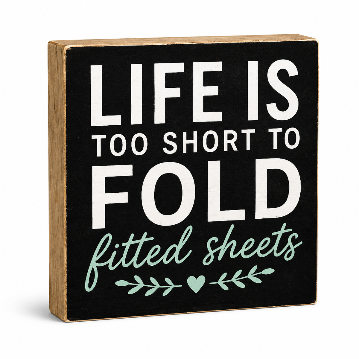 A square decorative wooden sign with a black front panel and natural wood sides. The sign reads “LIFE IS TOO SHORT TO FOLD” in large white letters, with “fitted sheets” in mint green script below, plus a small mint green leaf and heart motif.