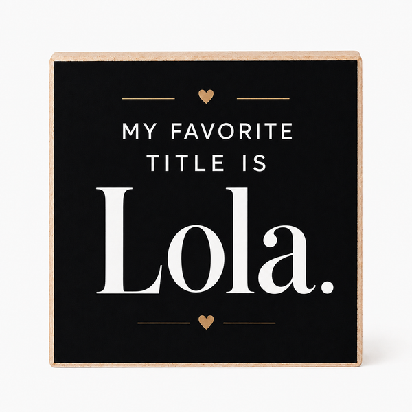 A square decorative sign with a black face and natural wood border, reading “MY FAVORITE TITLE IS Lola.” in white text with small gold heart and line accents, shown on a light gray background.