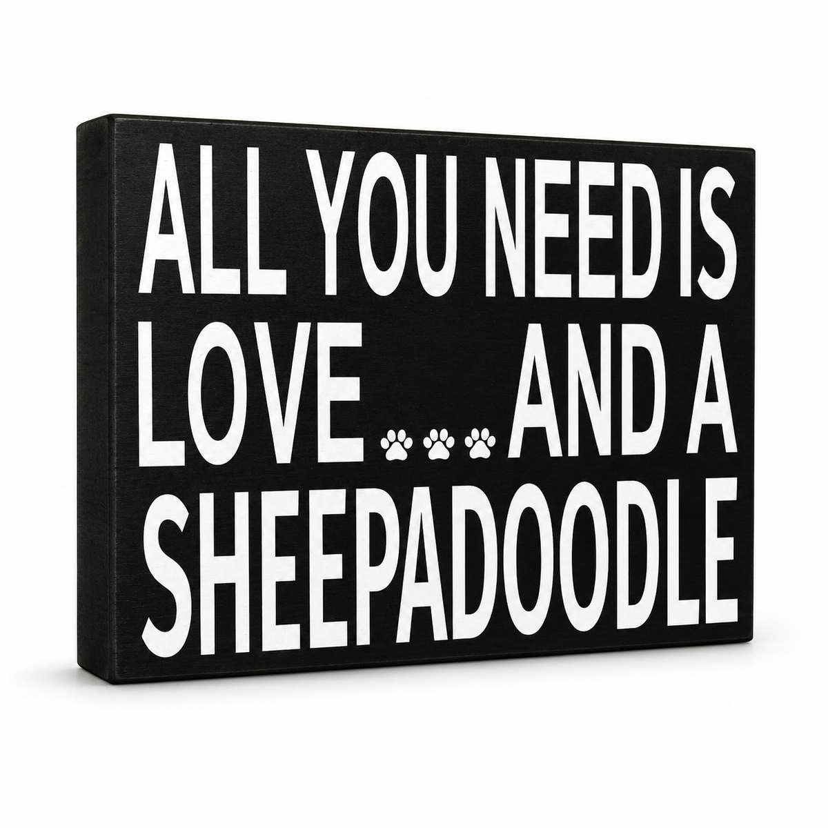A rectangular black canvas wall sign with bold white text reading 'ALL YOU NEED IS LOVE.