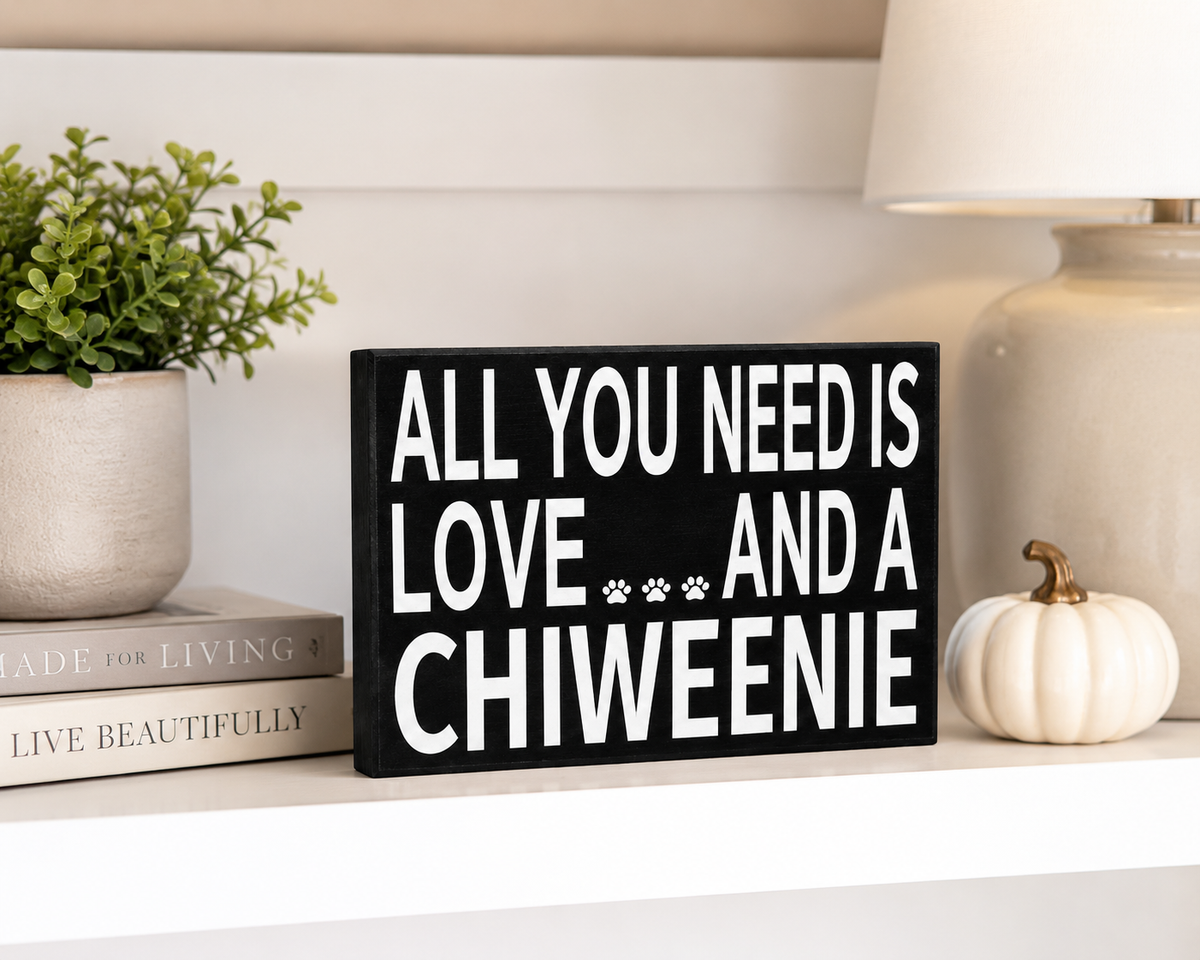 A black rectangular decorative sign with bold white text reading 'ALL YOU NEED IS LOVE.