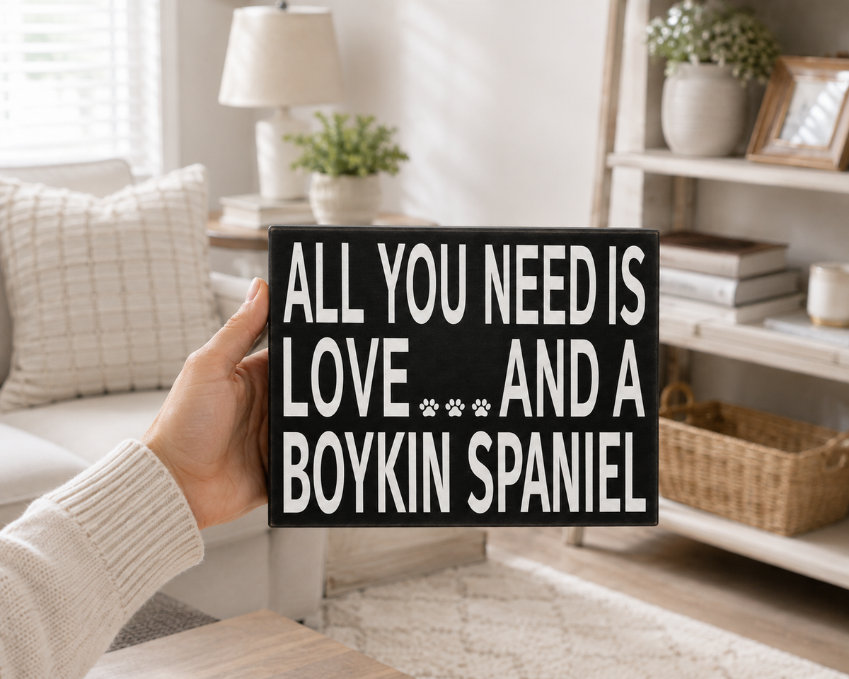 A hand holds a black decorative sign with white text that reads 'ALL YOU NEED IS LOVE.