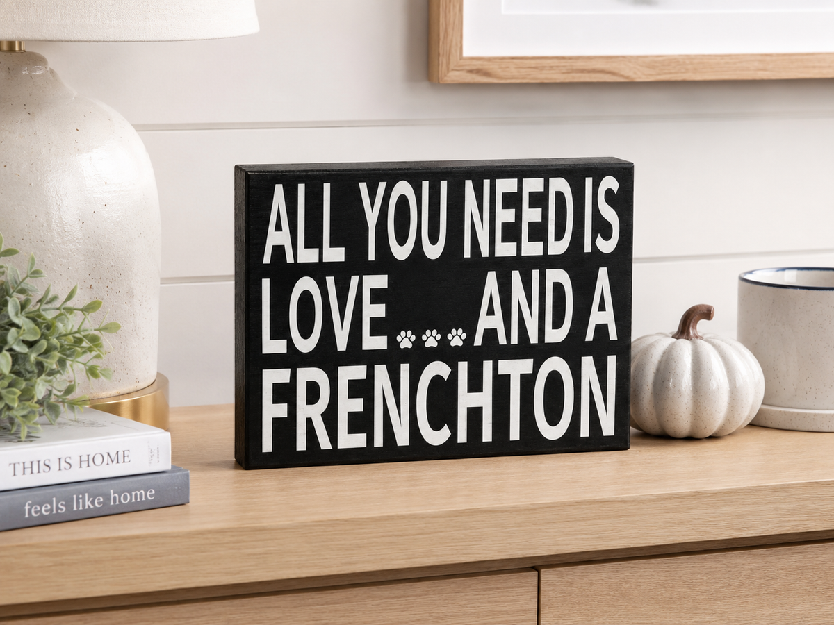 A rectangular black sign with bold white text reading 'ALL YOU NEED IS LOVE.