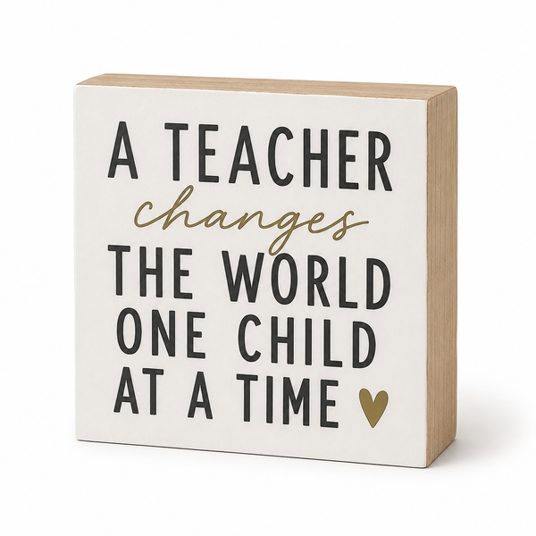 A square decorative wooden sign with a cream face and natural wood sides, featuring the text 'A TEACHER changes THE WORLD ONE CHILD AT A TIME' in black and gold lettering, with a small gold heart at the bottom right.