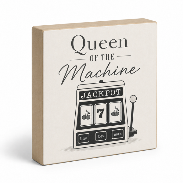 A square decorative block sign with a light beige wood-look frame and cream face, printed with the words 'Queen of the Machine' and a black-and-white slot machine illustration. The sign is photographed on a clean white background with a soft shadow.
