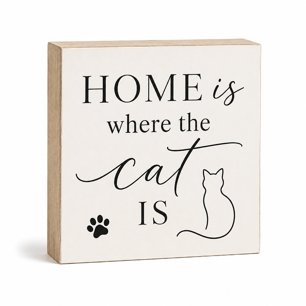 A square decorative wooden sign with a light natural wood border and an off-white face. The front is printed with the phrase “HOME is where the cat IS” in black serif and script lettering, plus a small black paw print and cat silhouette.