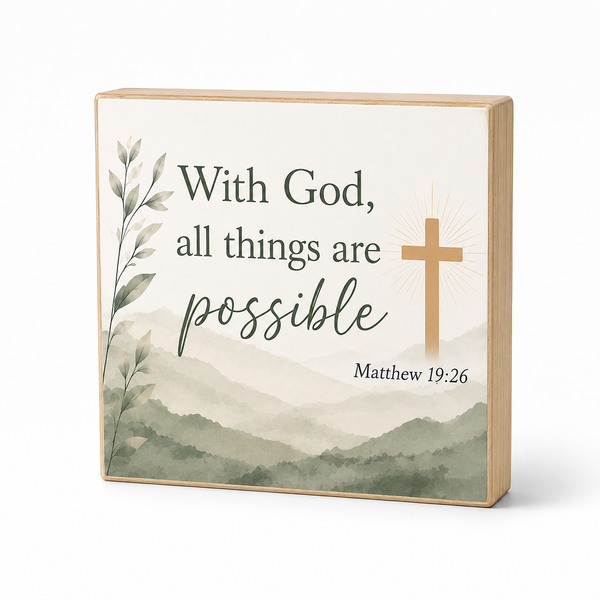 Square wooden wall art plaque with the phrase 'With God, all things are possible' and 'Matthew 19:26,' featuring a tan cross, muted mountain landscape, and leafy branch illustration on a white background.