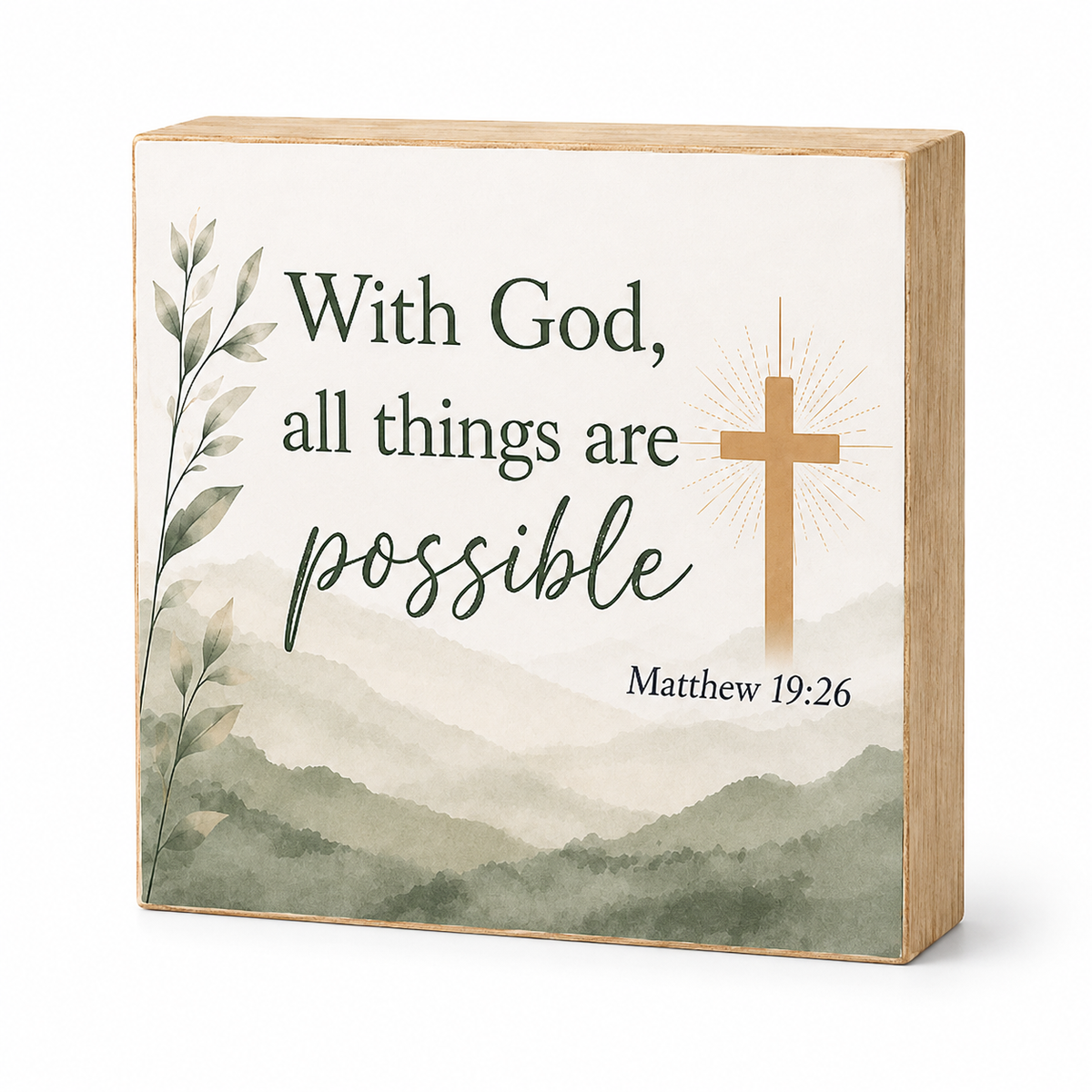 A square wooden decorative sign with a light natural wood border and front panel. The panel has a watercolor-style green mountain landscape, a tan cross with rays, and the text 'With God, all things are possible' and 'Matthew 19:26'.