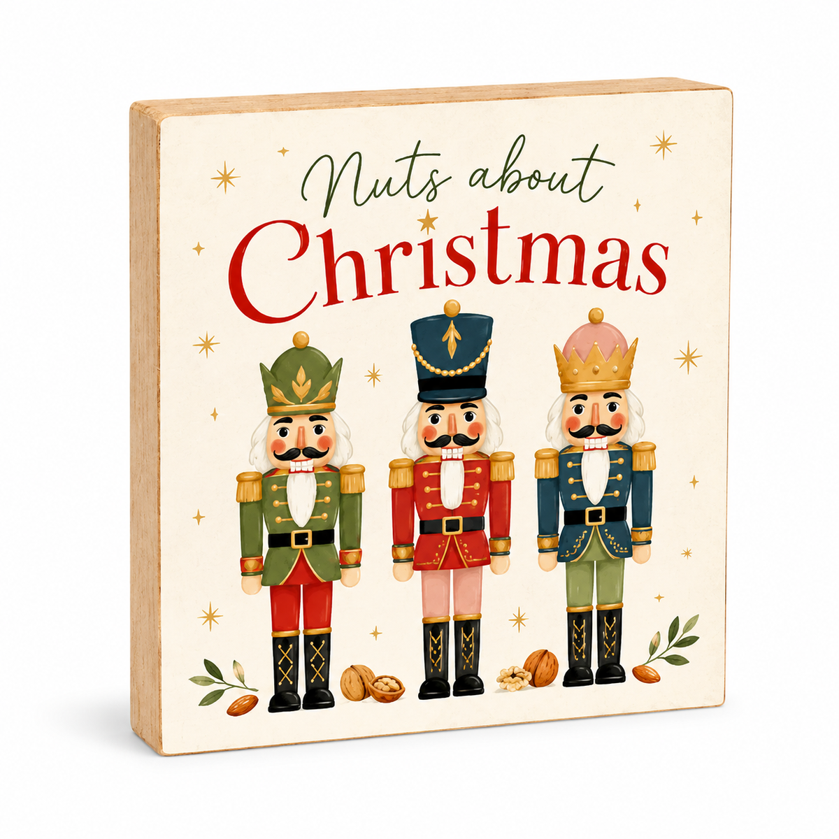 A square wooden Christmas sign with a light natural wood border and cream face, featuring the text 'Nuts about Christmas' in green and red script and illustration of three festive nutcracker figures in green, red, and blue uniforms with gold accents. Small gold stars, nuts, and leaves decorate the design.