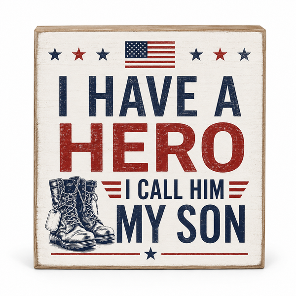 A square wooden decorative sign with a distressed patriotic design. The sign features the text 'I HAVE A HERO I CALL HIM MY SON' in navy blue and red lettering, an American flag at the top, and an illustration of combat boots at the bottom left.