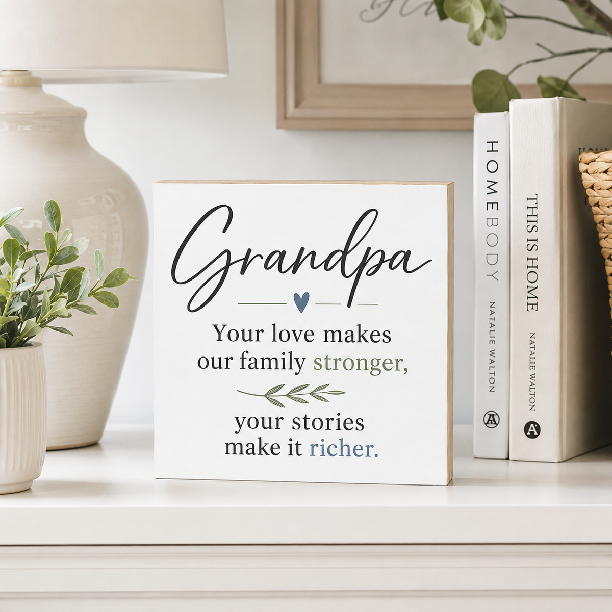 A white decorative wooden sign with printed text reading 'Grandpa' and a family message, styled on a shelf beside books and a ceramic vase.