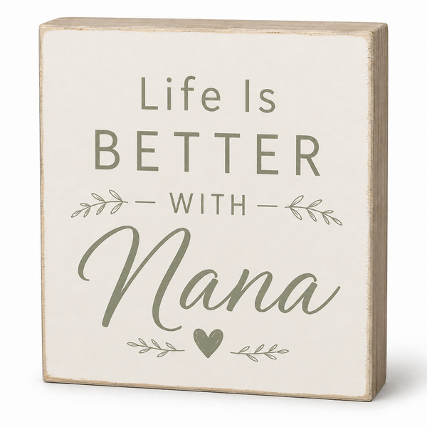 A square decorative wooden sign with a distressed cream face and natural wood edges. The sign features the text 'Life Is BETTER WITH Nana' in muted sage green lettering, accented with small leafy branches and a heart.