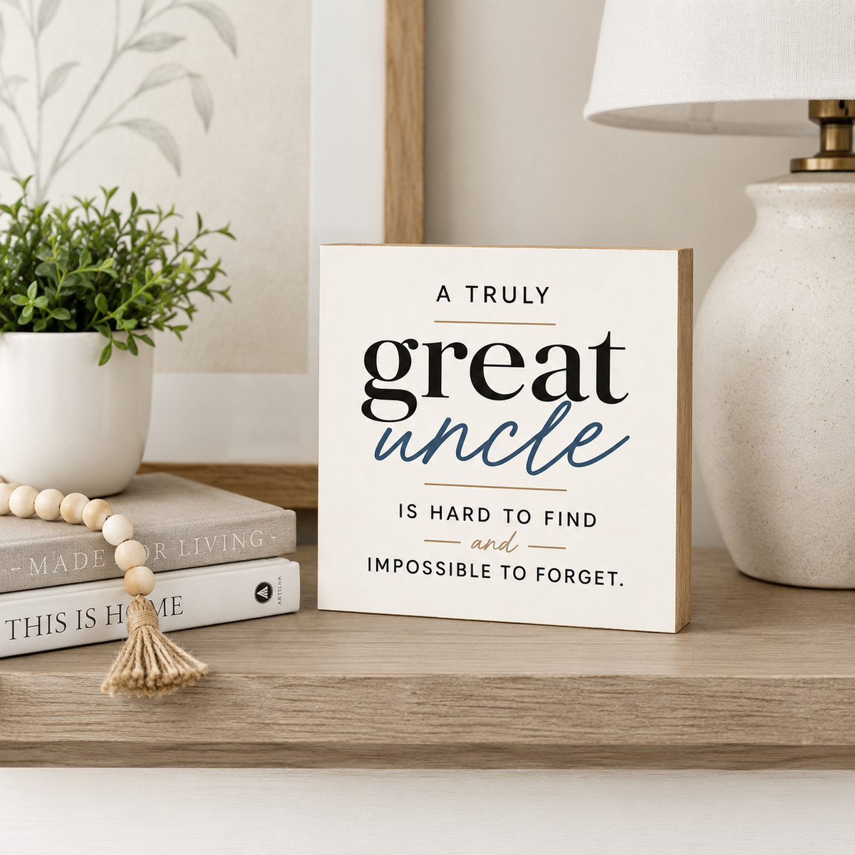 A square decorative sign with the phrase 'A TRULY great uncle IS HARD TO FIND and IMPOSSIBLE TO FORGET.' displayed on a wooden shelf beside a potted plant, books, a beaded tassel, and a lamp.