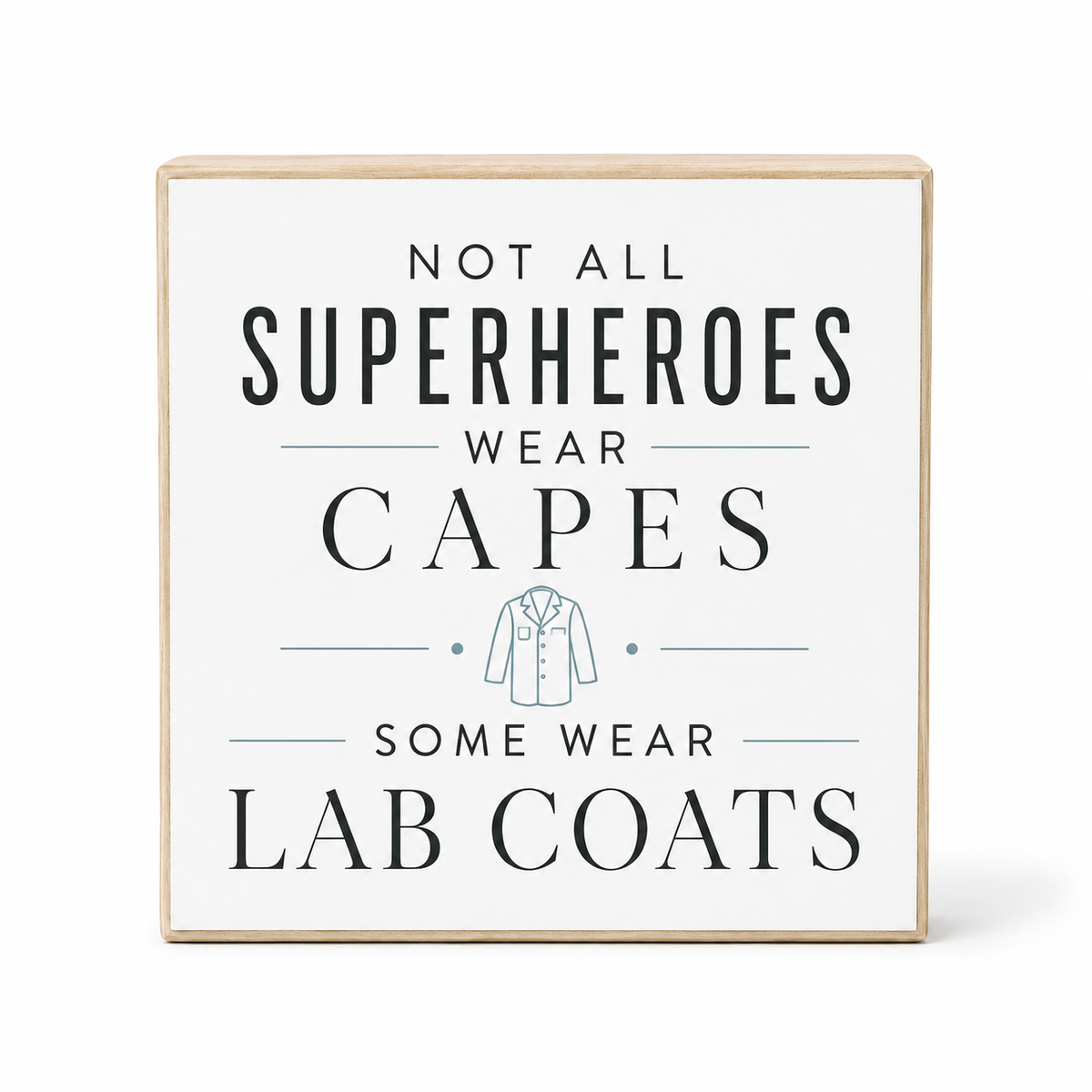 A square decorative wooden sign with a white face and natural wood border, featuring the text 'NOT ALL SUPERHEROES WEAR CAPES SOME WEAR LAB COATS' in dark lettering with a small lab coat illustration, shown on a light gray background.