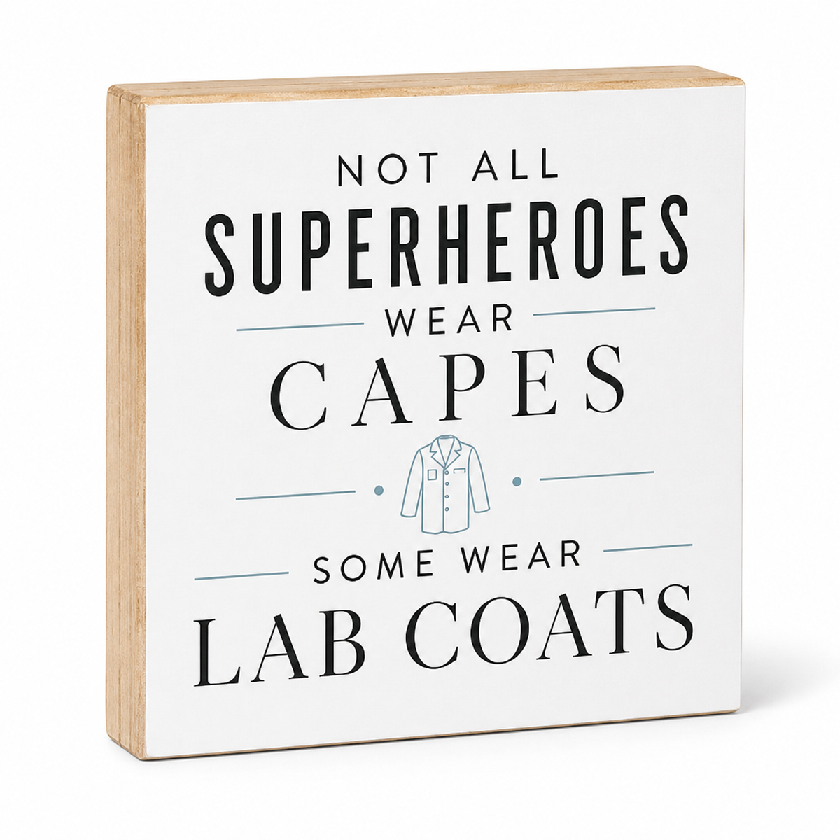A square decorative wooden sign with a white front and natural wood sides, printed with the phrase 'NOT ALL SUPERHEROES WEAR CAPES SOME WEAR LAB COATS' in black text with a small light blue lab coat illustration.