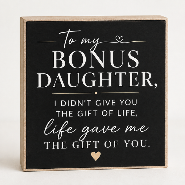 A square decorative sign with a black face and natural wood border, featuring white and light beige text that reads, 'To my BONUS DAUGHTER, I DIDN'T GIVE YOU THE GIFT OF LIFE, life gave me THE GIFT OF YOU.' with small heart accents, shown on a light neutral background.