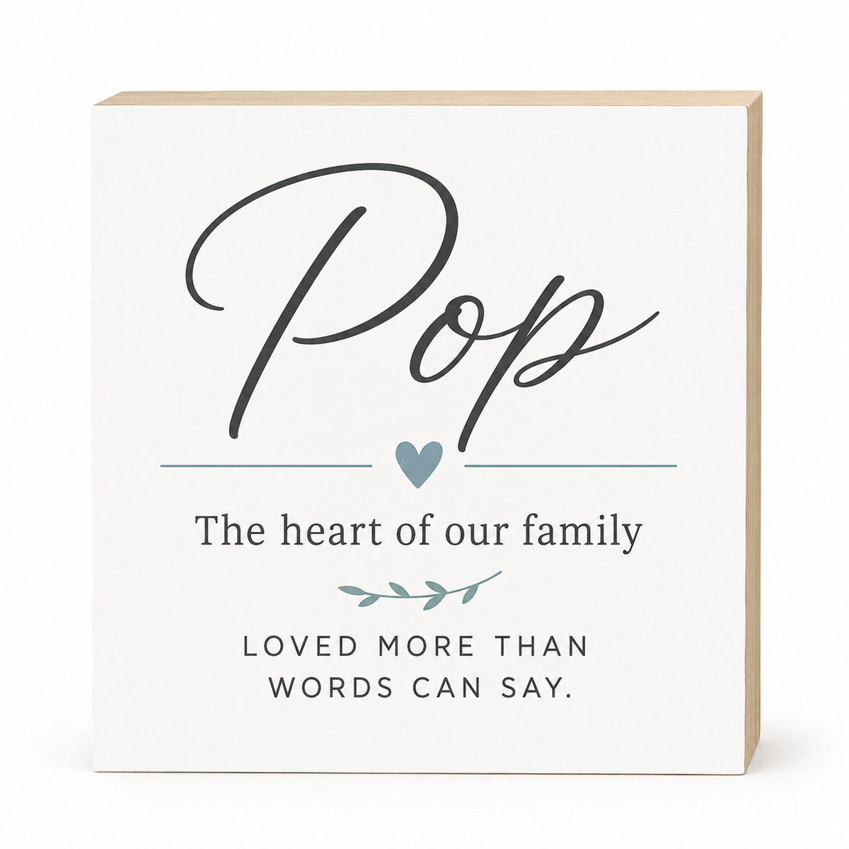 A square white decorative sign with a light wood edge, featuring the word 'Pop' in large black script, a small blue heart, and the phrases 'The heart of our family' and 'LOVED MORE THAN WORDS CAN SAY.' on a clean white background.