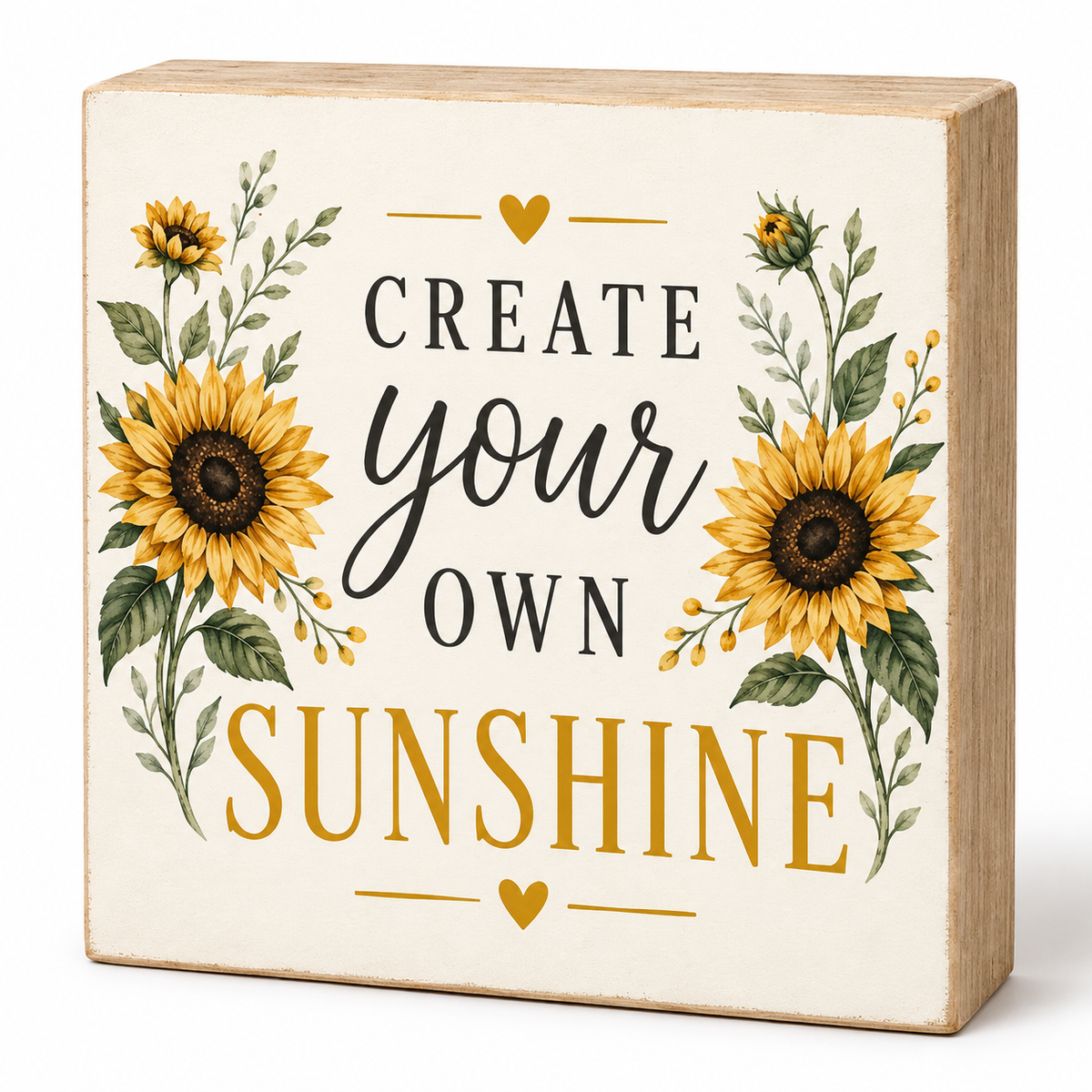 A square decorative wooden block sign with a cream face, featuring the phrase 'CREATE your OWN SUNSHINE' in black and mustard lettering, surrounded by illustrated sunflowers and green foliage. The side of the block is light natural wood.