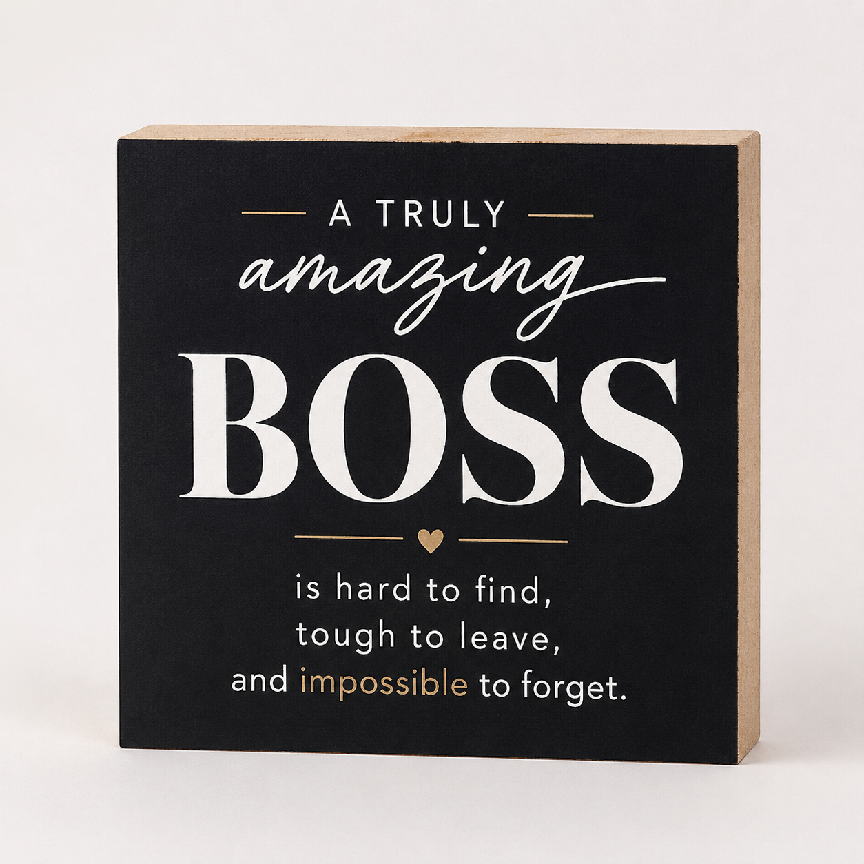 A square decorative wall sign with a black front and natural wood sides, featuring the phrase 'A TRULY amazing BOSS is hard to find, tough to leave, and impossible to forget.' in white and gold lettering, shown on a light neutral background.