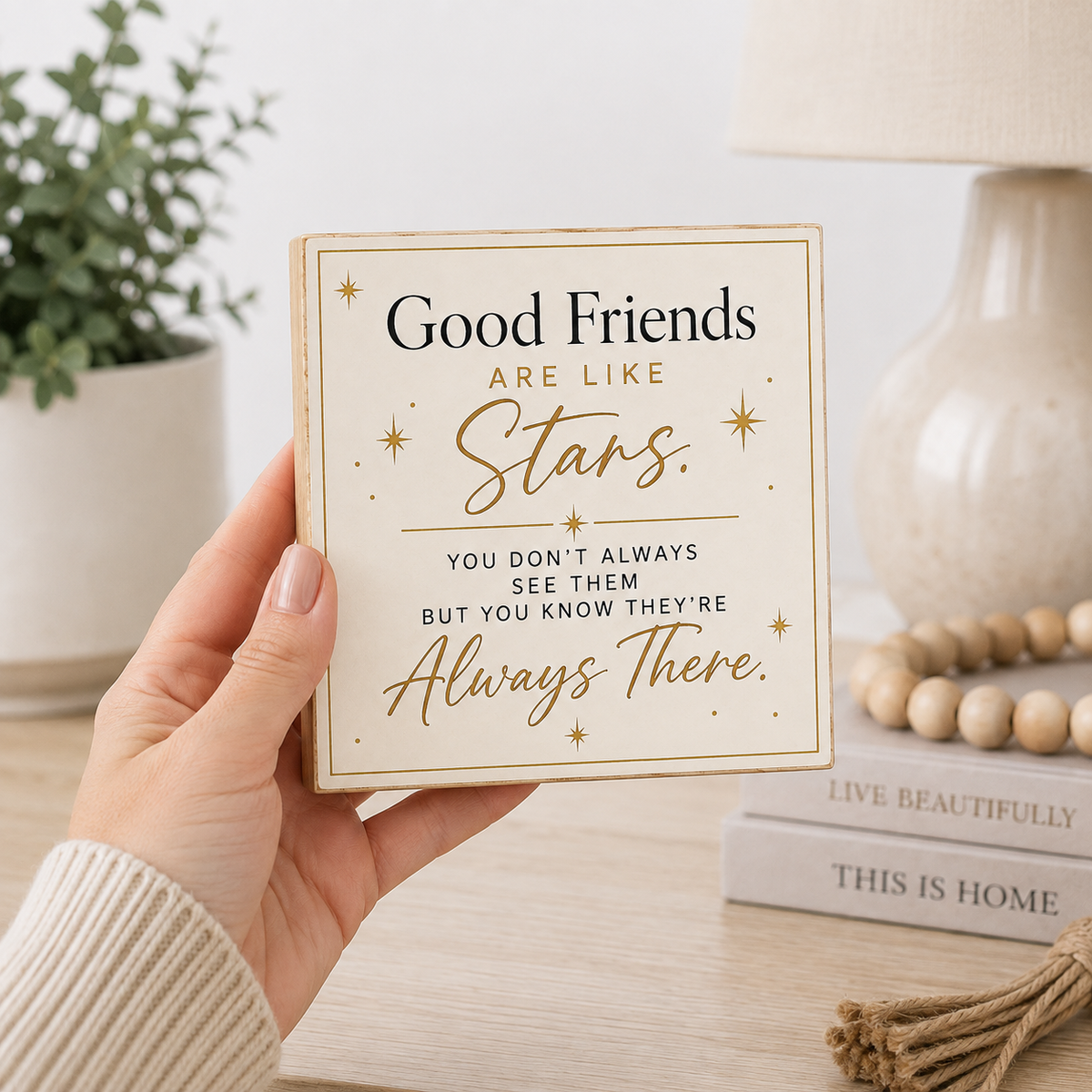 A hand holds a square decorative sign with the quote 'Good Friends ARE LIKE Stars. YOU DON'T ALWAYS SEE THEM BUT YOU KNOW THEY'RE Always There.
