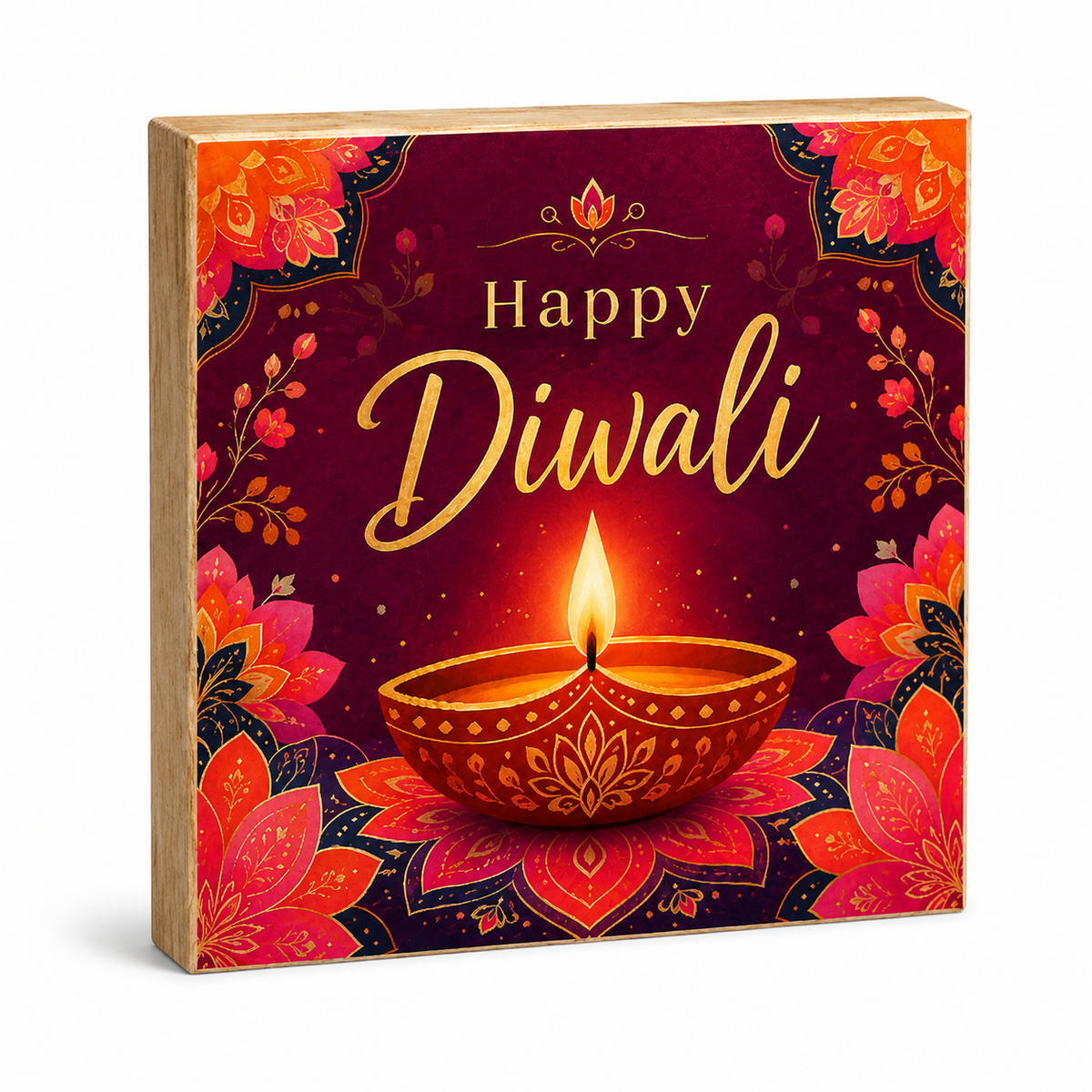 A square wooden decorative box featuring a festive Diwali design with the words 'Happy Diwali' in gold script, a glowing diya oil lamp, and ornate floral mandala patterns in red, orange, pink, and gold on a dark background.