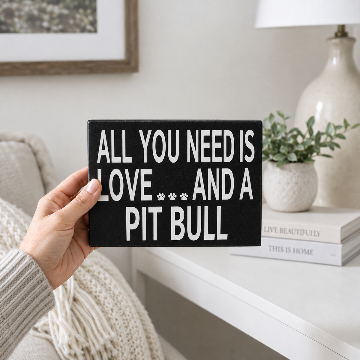 A hand holds a black rectangular sign with white text that reads 'ALL YOU NEED IS LOVE.