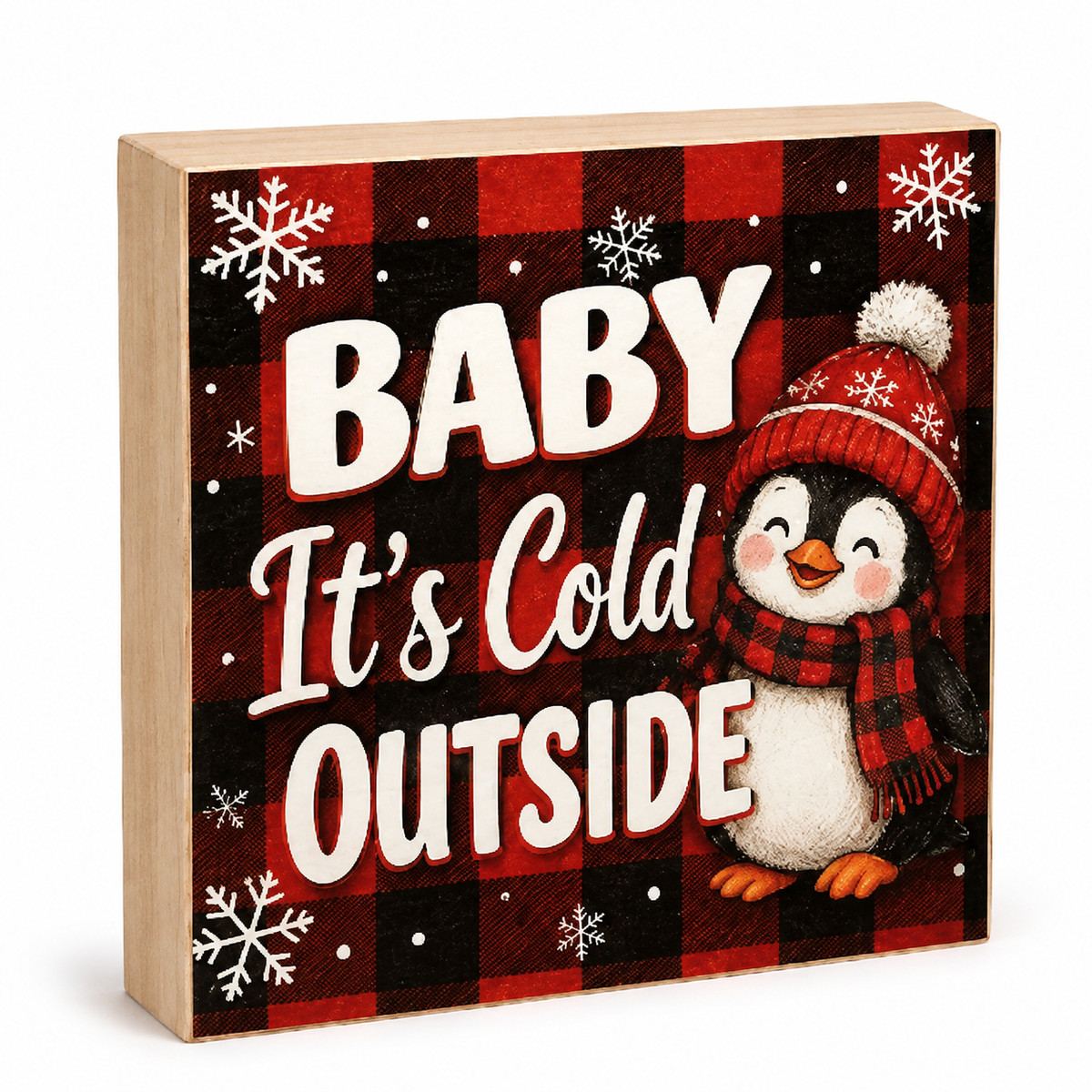 A square wooden decorative sign with a red and black buffalo plaid pattern, white snowflakes, and the text 'BABY It's Cold OUTSIDE' in large white letters. A penguin wearing a red plaid hat and scarf stands on the right side.