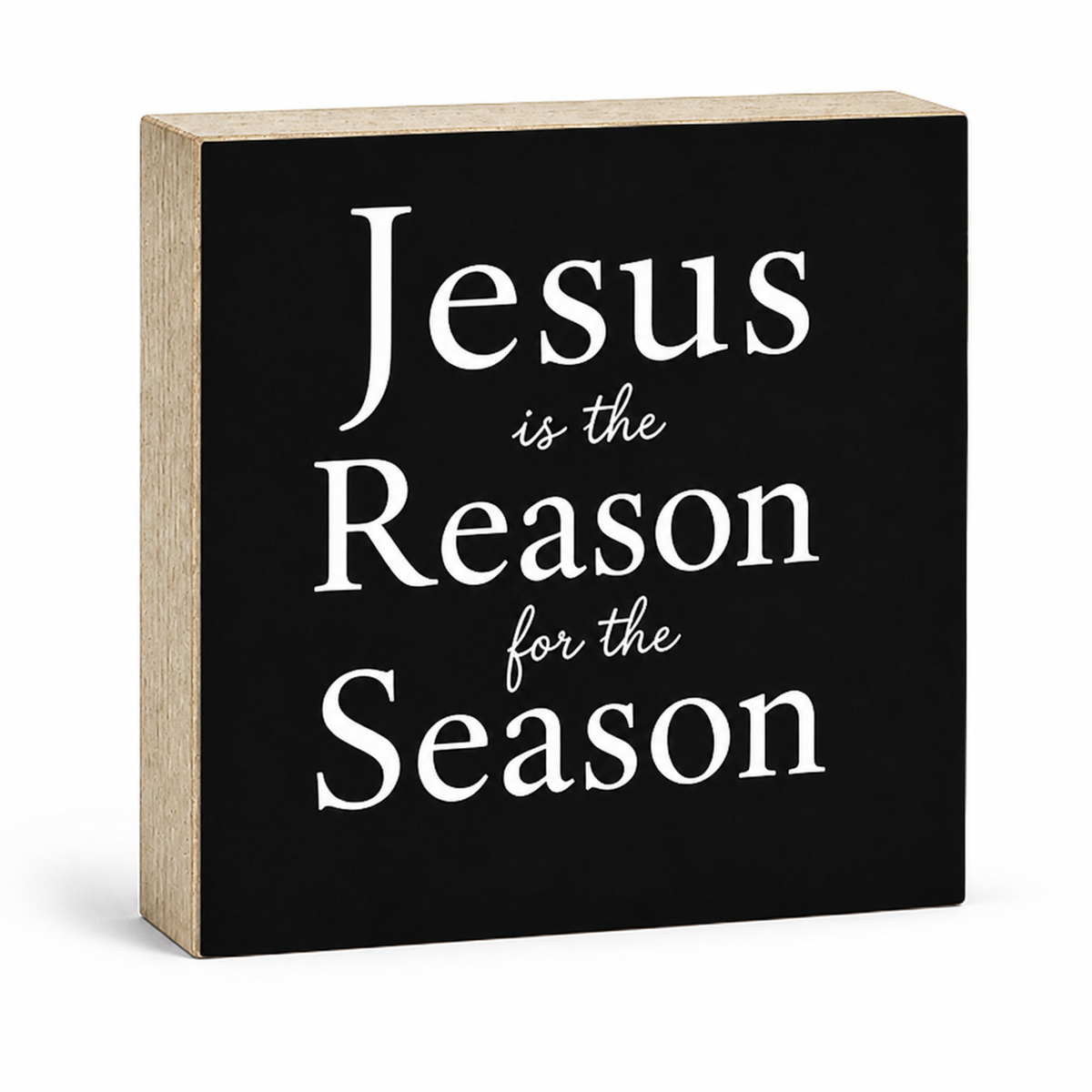 A square decorative wooden sign with a black front panel and natural wood sides, featuring the phrase 'Jesus is the Reason for the Season' in white lettering, shown on a white background.