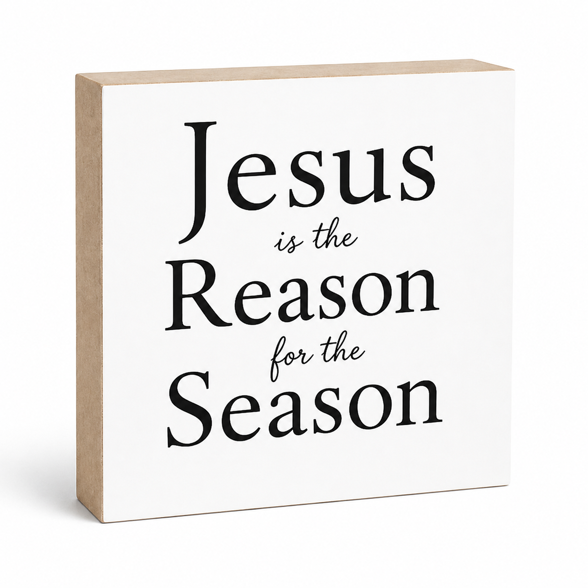 A square decorative wall sign with a white front and natural wood side edges. The front is printed with the phrase “Jesus is the Reason for the Season” in large black serif and script text.