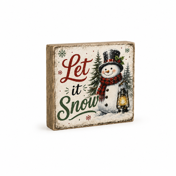 A square rustic wooden decorative sign featuring the phrase 'Let it Snow' in red and green script, with an illustrated snowman wearing a black top hat and red plaid scarf next to a lit lantern and small evergreen trees.