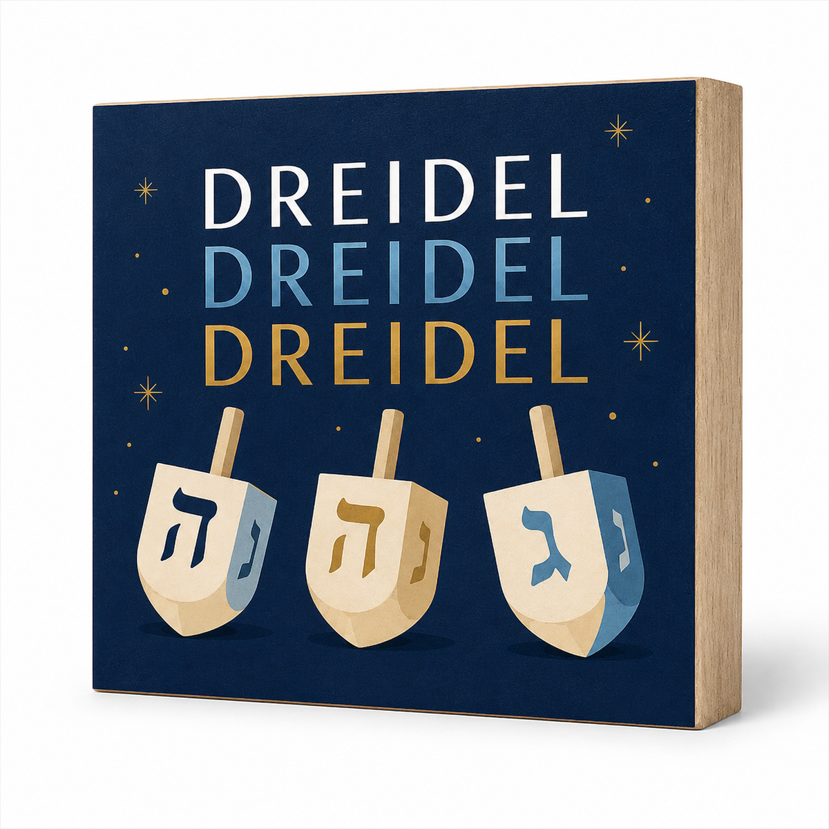 A square decorative sign with a light wood edge and a navy blue face, featuring the word 'DREIDEL' repeated three times in white, light blue, and gold, above three illustrated dreidels in beige, light blue, and navy. The sign is photographed on a clean white background.