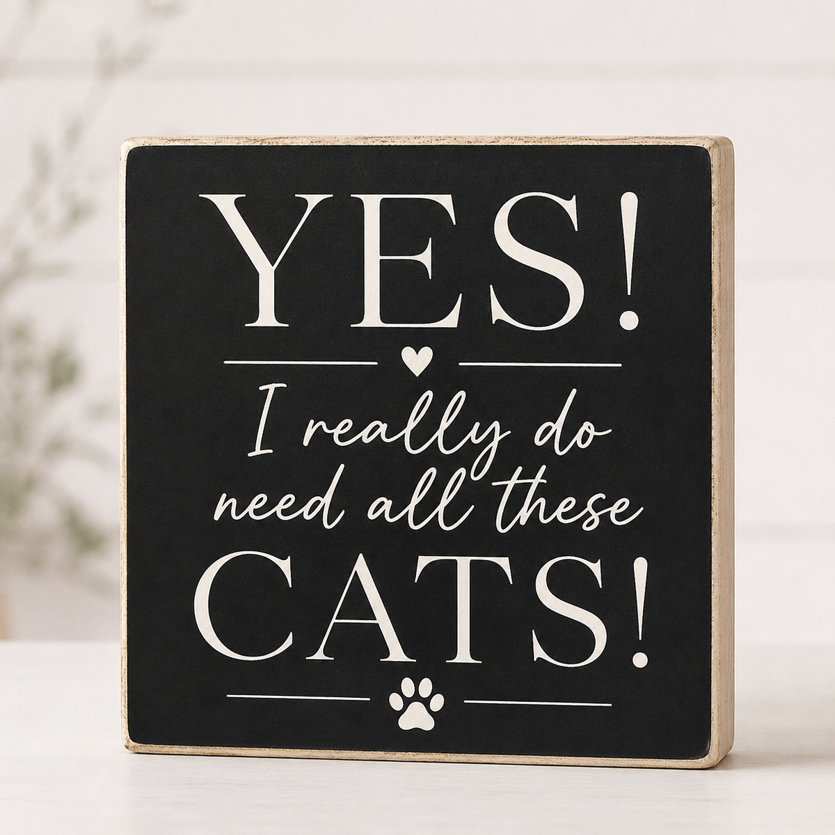 A square decorative wooden sign with a black face and natural wood edges, printed with the phrase “YES! I really do need all these CATS!” in white lettering, with a small paw print at the bottom, shown on a light surface.