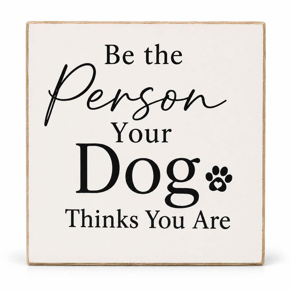 A square decorative wooden sign with a light beige wood-grain border and a cream background. The sign features black printed text that reads 'Be the Person Your Dog Thinks You Are' along with a small black paw print icon.