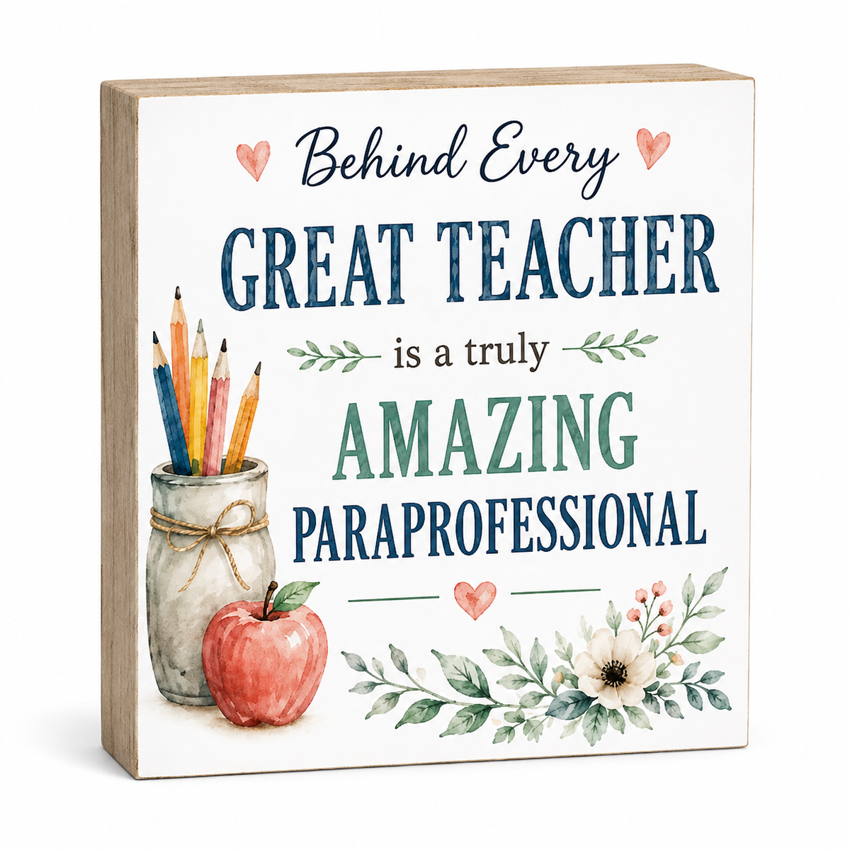 A square decorative sign with a light wood border and a white face, printed with the phrase 'Behind Every GREAT TEACHER is a truly AMAZING PARaprofessional' in blue and green lettering, with small watercolor illustrations of hearts, pencils in a jar, an apple, and floral leaves. The sign is photographed on a clean white background.