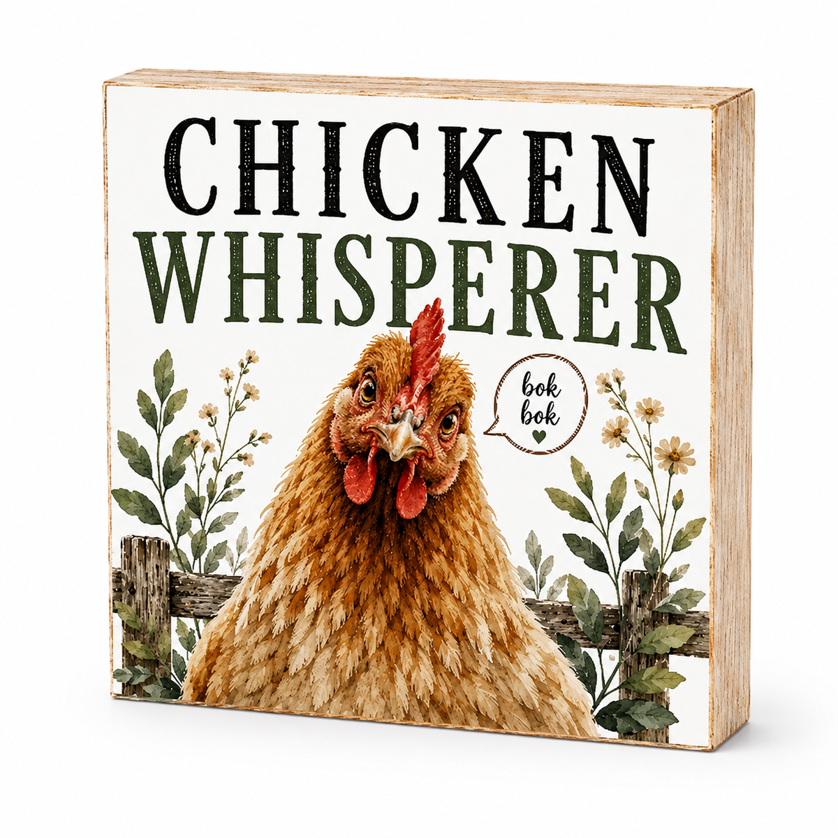 A square decorative wooden sign with a rustic finish, featuring an illustration of a brown hen, green text reading 'CHICKEN WHISPERER', and a speech bubble that says 'ook bok'.