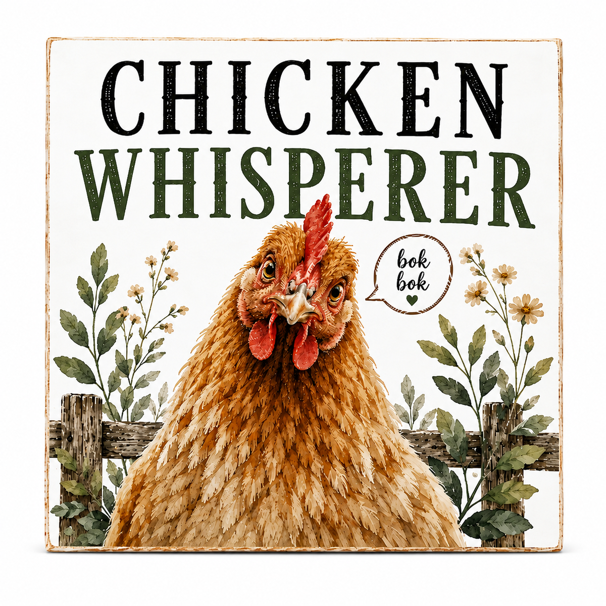 A square decorative sign with a rustic white background featuring the words “CHICKEN WHISPERER” in large black and dark green lettering above an illustrated brown hen with a red comb and a small speech bubble that says “bok bok.” Floral plants and a wooden fence decorate the lower portion.
