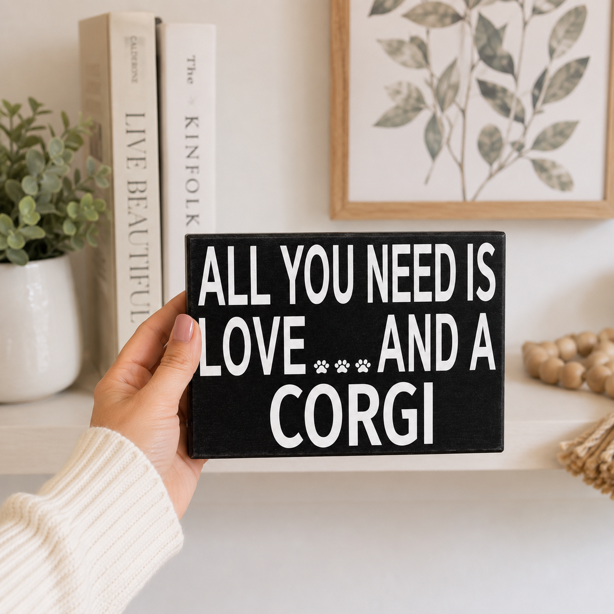A hand holding a black rectangular sign with white text that reads 'ALL YOU NEED IS LOVE.