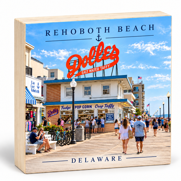 A square wooden block sign featuring a printed photograph of Rehoboth Beach in Delaware, with large red 'Doller's' signage and the words 'REHOBOOTH BEACH' and 'DELAWADE' on the front.