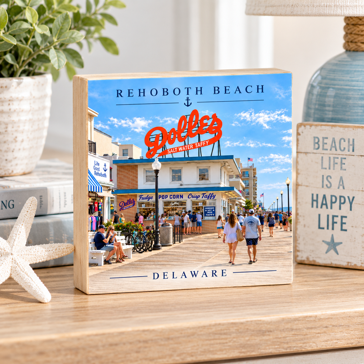 A personalized wooden block sign featuring a photo print of Rehoboth Beach, Delaware, styled on a wooden tabletop with a potted plant, books, and a starfish.