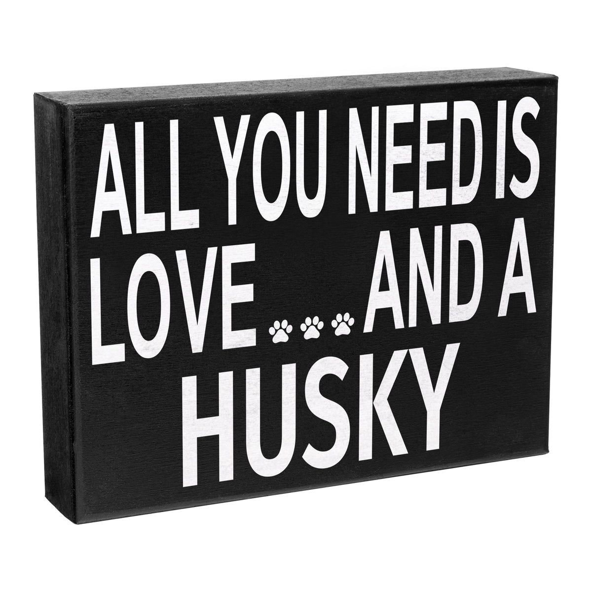 A black wooden box sign with the text 'All You Need is Love and a HUSKY' in white capital letters, with a paw print symbol after the word 'HUSKY'. The sign is rectangular and has a solid black background.