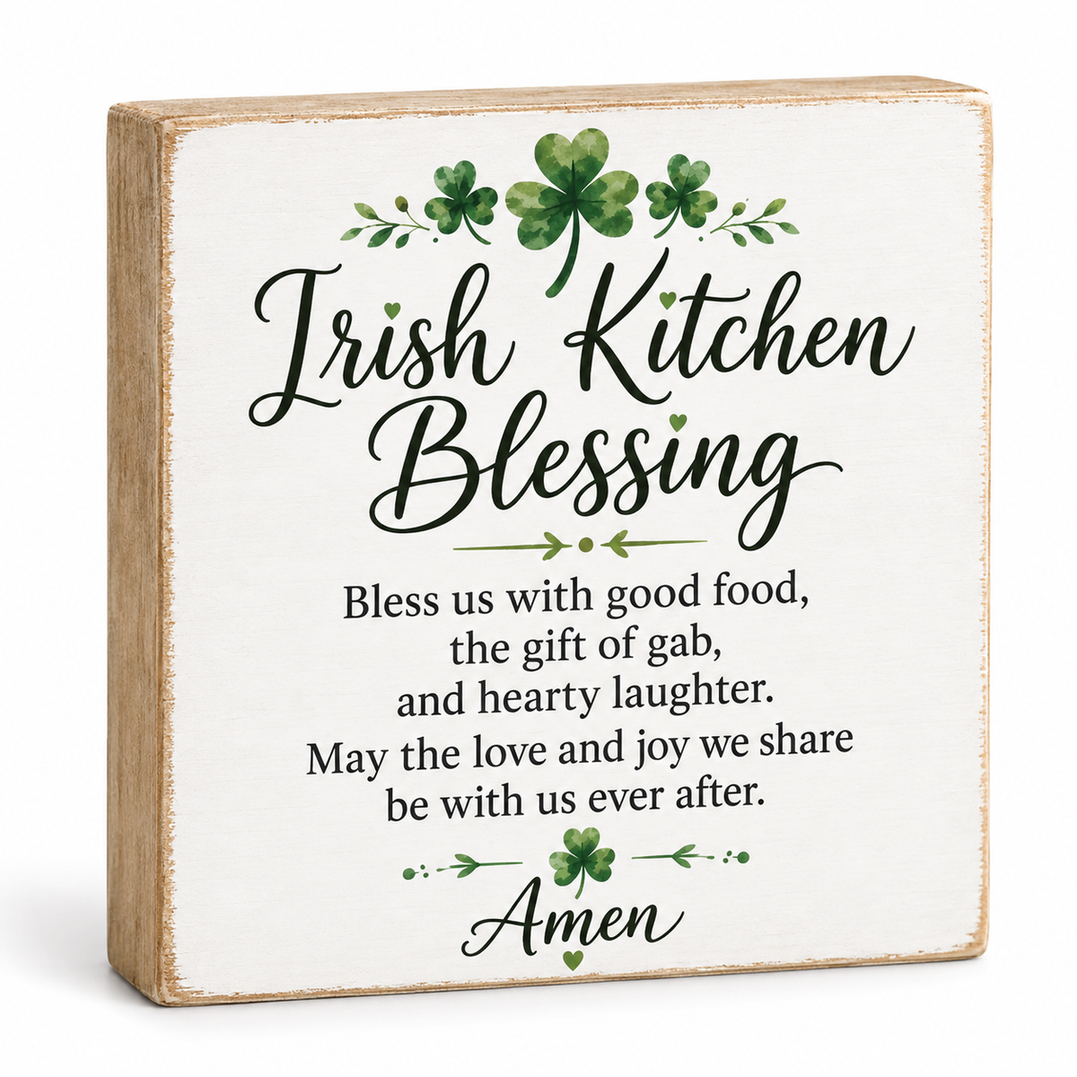 A square decorative wooden sign with a distressed white face and natural wood edges, printed with the phrase 'Irish Kitchen Blessing' and a poem beneath it in black script and serif text, accented with green shamrock illustrations.