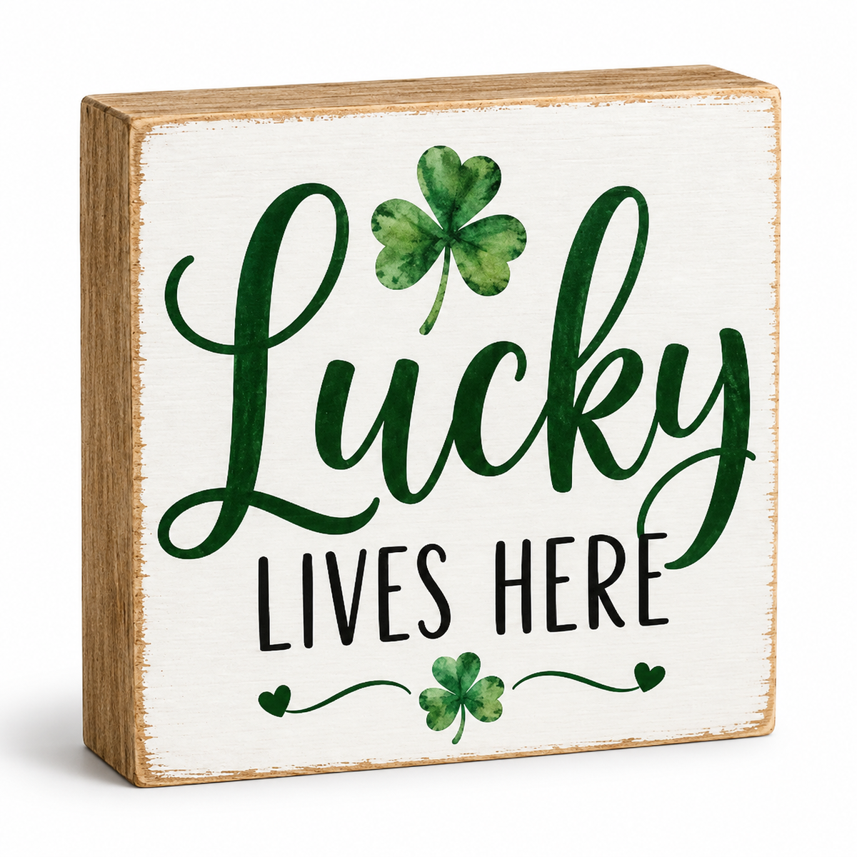 A square wooden decorative sign with a whitewashed face and natural wood edges. The sign reads 'Lucky Lives Here' in dark green and black lettering, decorated with green shamrock motifs, on a clean white background.