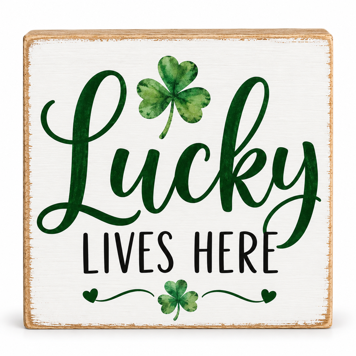 A square decorative wooden sign with a distressed white painted face, a natural wood border, and the phrase “Lucky Lives Here” in dark green and black lettering, accented with two green shamrocks.