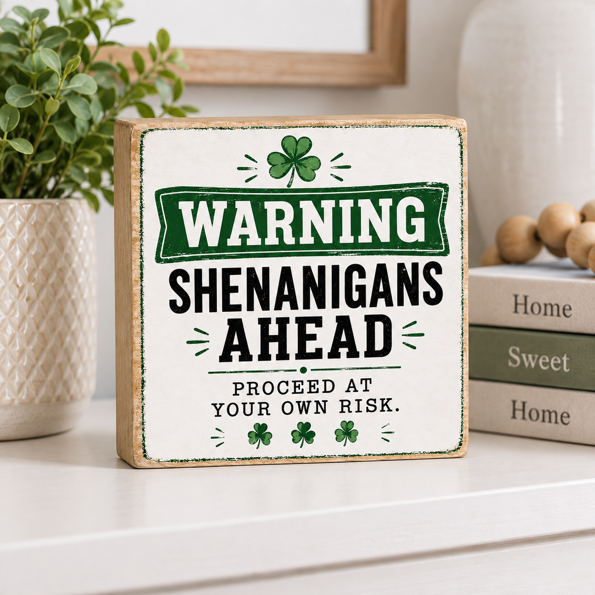 A square wooden sign with a distressed white face and natural wood edges, featuring a green and black St. Patrick's Day warning sign that reads 'WARNING SHENANIGANS AHEAD PROCEED AT YOUR OWN RISK.