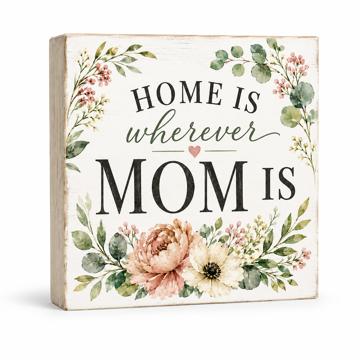 A square decorative wooden sign with a distressed white front, featuring the phrase 'HOME IS wherever MOM IS' in black and green lettering, surrounded by watercolor-style flowers and greenery. The side of the block shows a natural light wood tone.